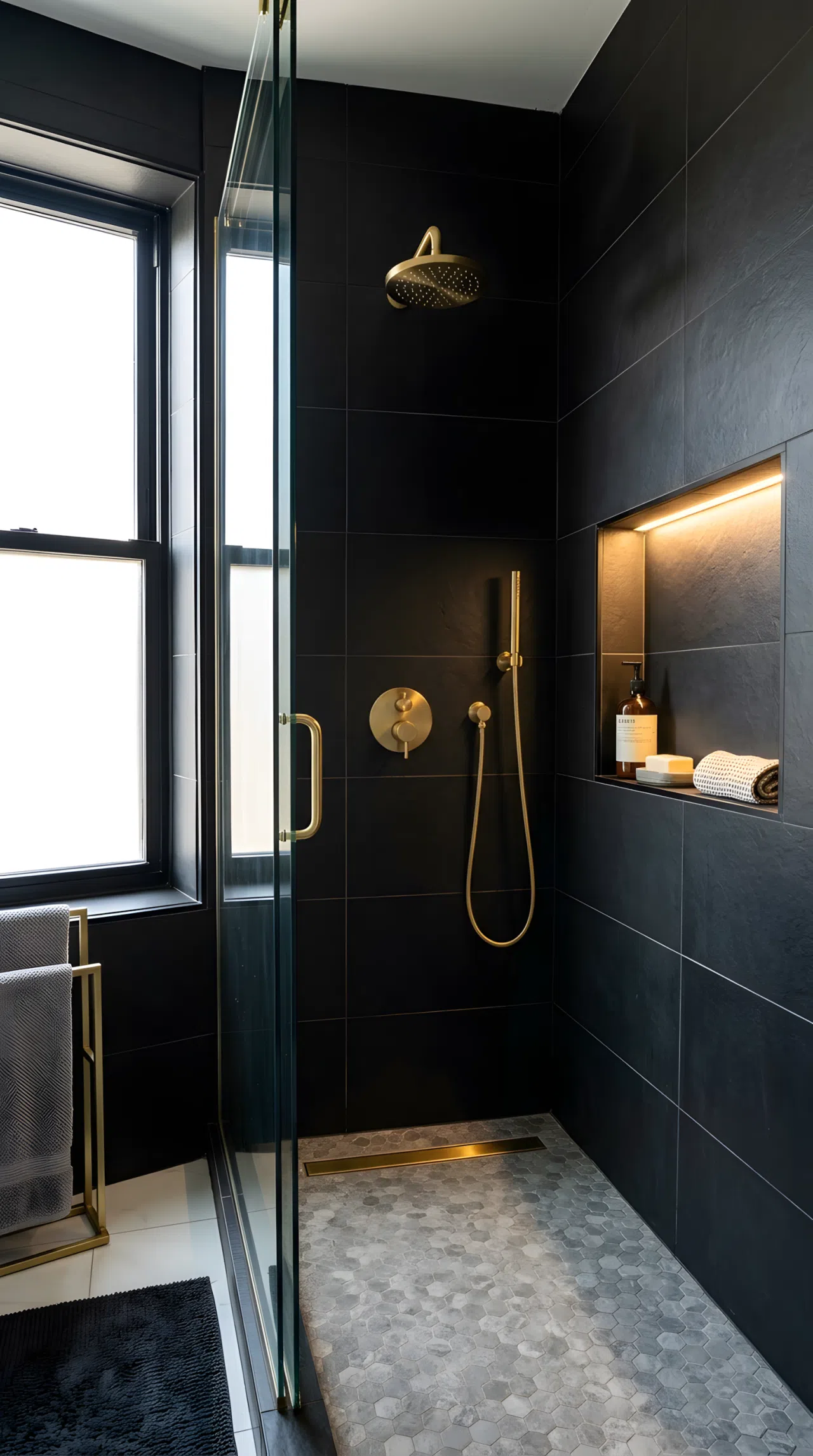 Real-life photo of an apartment bathroom shower with matte black tile walls (RGB 28,28,30), a small waterproof light fixture glowing inside the shower niche illuminating the corner evenly, brass showerhead, clean organized styling, bright natural light entering from a nearby window, vibrant contrast, stock photography style.