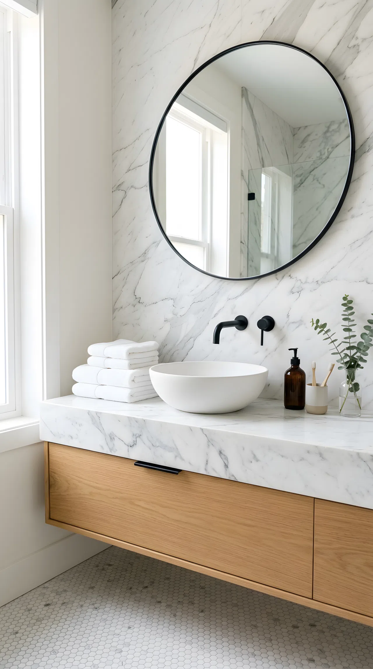 Real-life photograph of a bathroom vanity with white and gray marble slab running seamlessly from the countertop up the wall as a backsplash, continuous veining pattern, single vessel sink, matte black faucet, neatly organized counter with folded white towels, bright natural light, clean editorial stock photo style, no render.