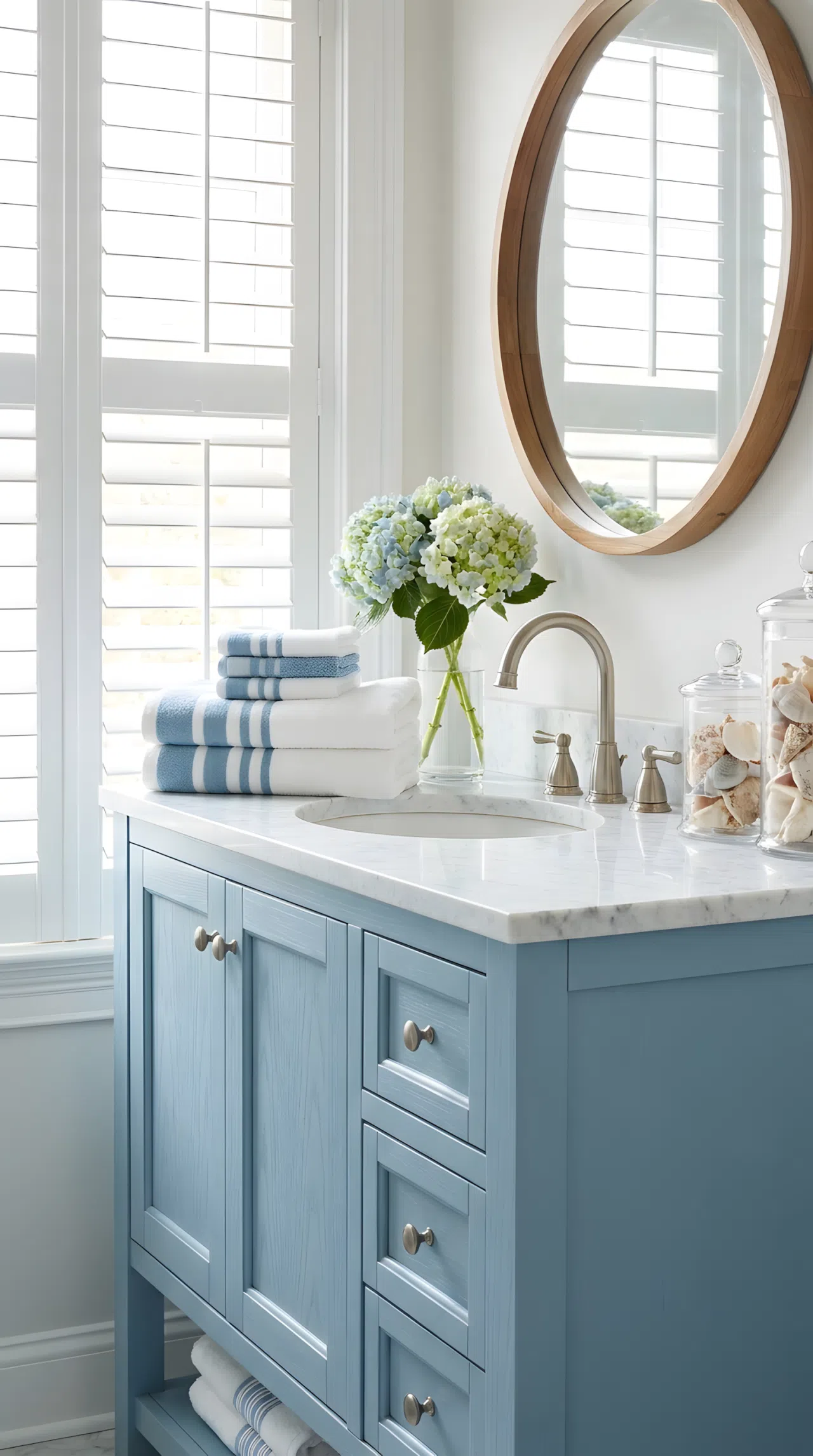 Real-life bathroom with a coastal blue vanity cabinet (RGB 143,176,196), white marble countertop, brushed nickel faucet, neatly made and beautifully arranged towels stacked beside the sink, bright natural light coming through a nearby window highlighting the vanity color, clean and organized styling, photography style, vibrant tones.