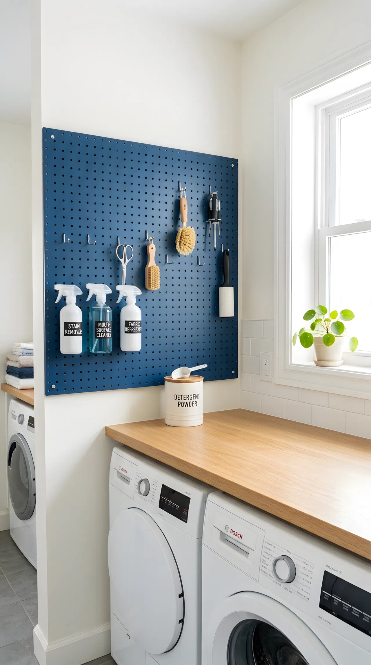 A laundry room wall with a deep blue painted pegboard (#274B7D) neatly hung with spray bottles, small tools, and a lint brush on labeled hooks, clear counter below, beautifully arranged, organized, clean, bright natural light, real-life photography, not a render, vibrant blue pegboard, Pinterest-style stock photo
