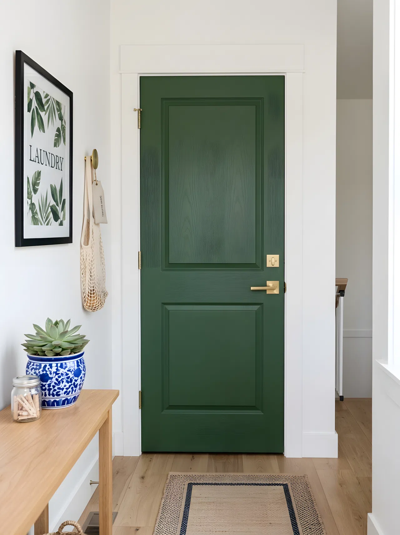 Real-life photograph of a laundry room entryway with a hunter green painted door (#355E3B), crisp white trim and walls, brushed brass door handle, clean and neatly finished space, bright natural light, vibrant accent color, stock-photography style, no illustration, no 3D render.