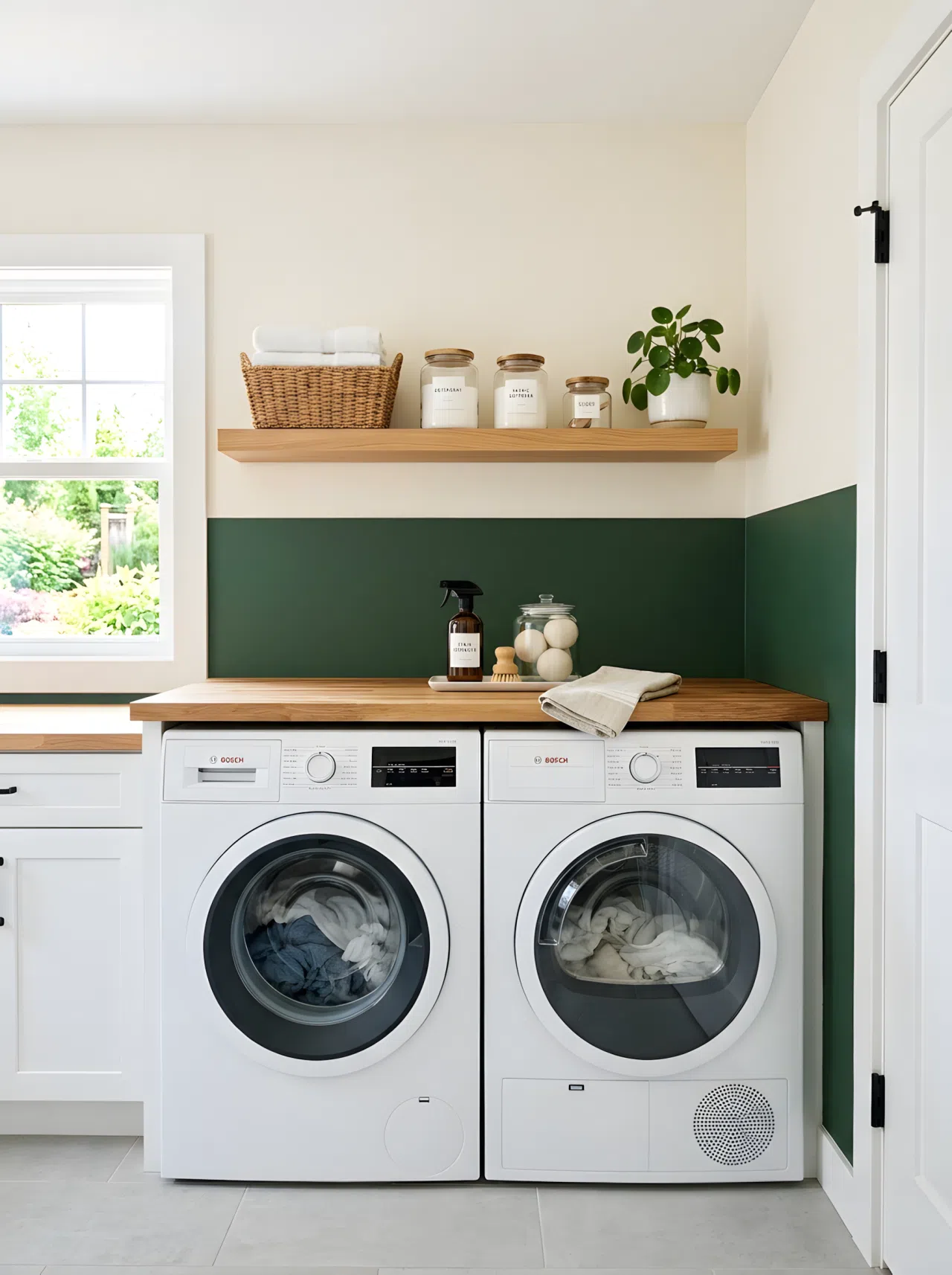 Real-life photograph of a laundry room wall painted deep green (#2E4E3F) on the lower third and soft cream (#F2EDE4) above, crisp clean paint line, neatly organized washer and dryer below, bright natural light, vibrant contrast, stock-photography style, no illustration, no 3D render.