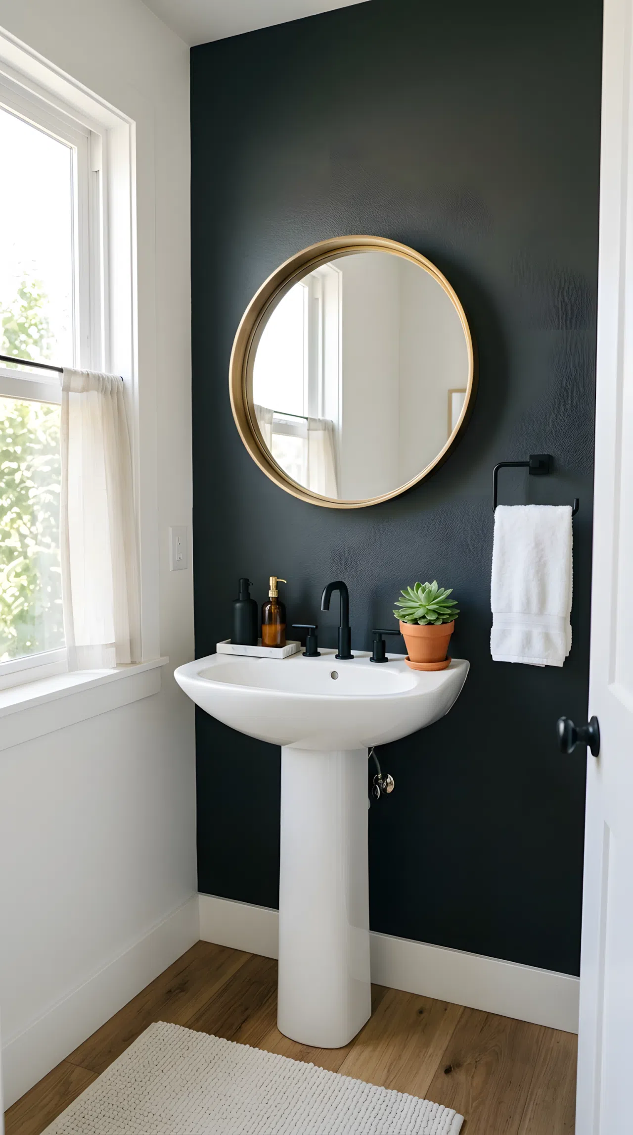 Real-life stock photo of a small guest bathroom with one deep charcoal accent wall (RGB 54,58,61) behind a white pedestal sink, matte black faucet, brass mirror frame, neatly made white hand towel folded on a rack, organized clean countertop, bright natural light streaming from a side window, vibrant warm accents from a small potted plant, Pinterest-ready aesthetic, photographed with a DSLR, no illustration, no 3D render.