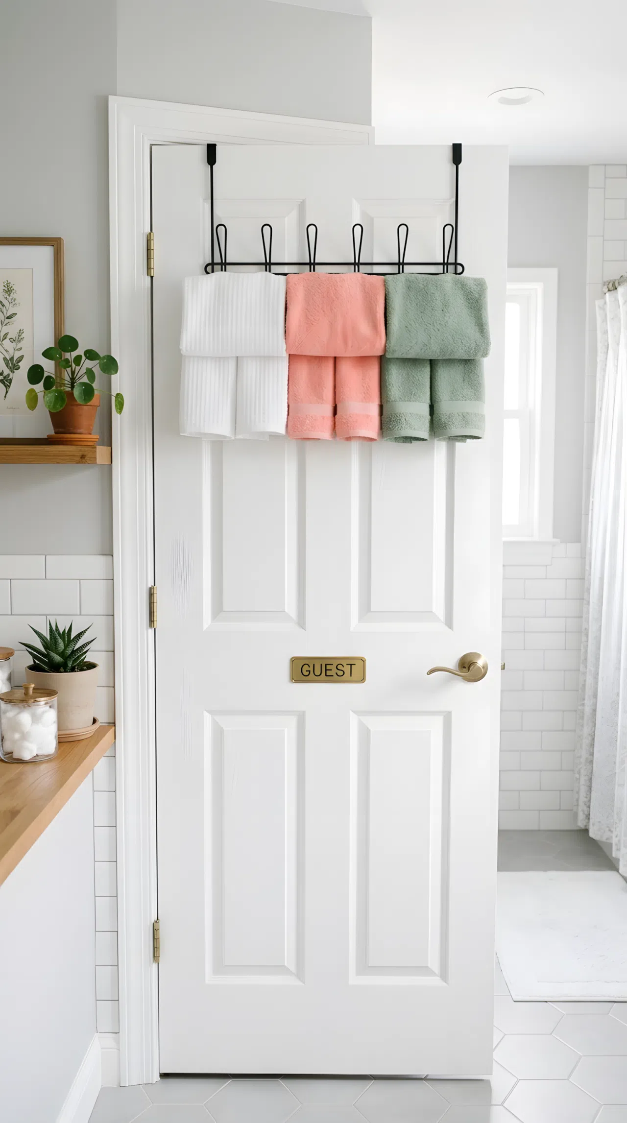 Real-life stock photo of a small guest bathroom door with an over-the-door hook rack, neatly folded white and beige towels hanging on each hook, organized and tidy, clean white door, bright natural light, vibrant towel color accents, Pinterest-ready styling, photographed like a home organization magazine, no illustration, no 3D render.