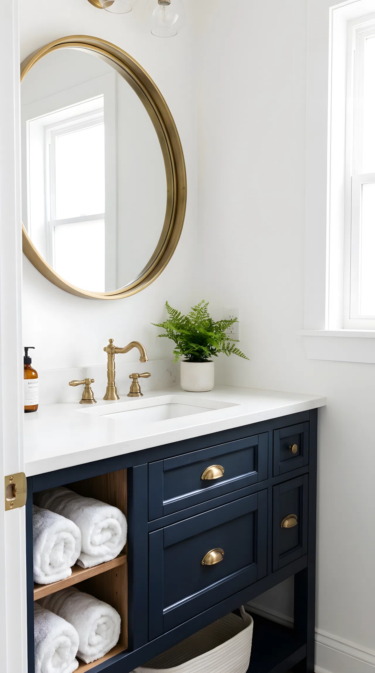 Real-life photo of a small hallway bathroom with a navy blue vanity (RGB 30, 58, 95), brass faucet and hardware, large round mirror, white walls, bright natural light, beautifully arranged, organized, clean, vibrant rich navy tone, stock photography style.