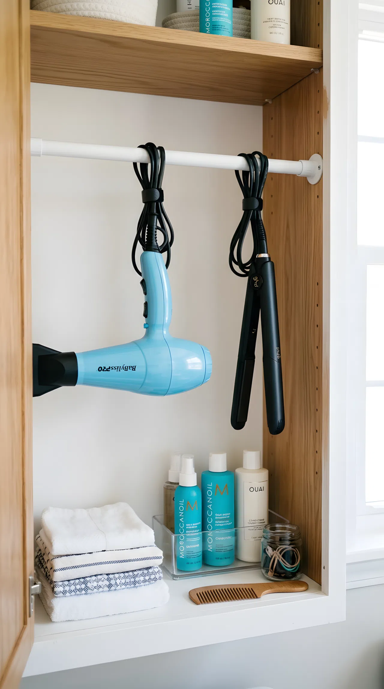 Inside a bathroom cabinet, a tension rod mounted horizontally with a hair dryer and straightener hanging by their cords, neatly organized, clean, bright natural light, real-life photography, vibrant colors, Pinterest-ready.
