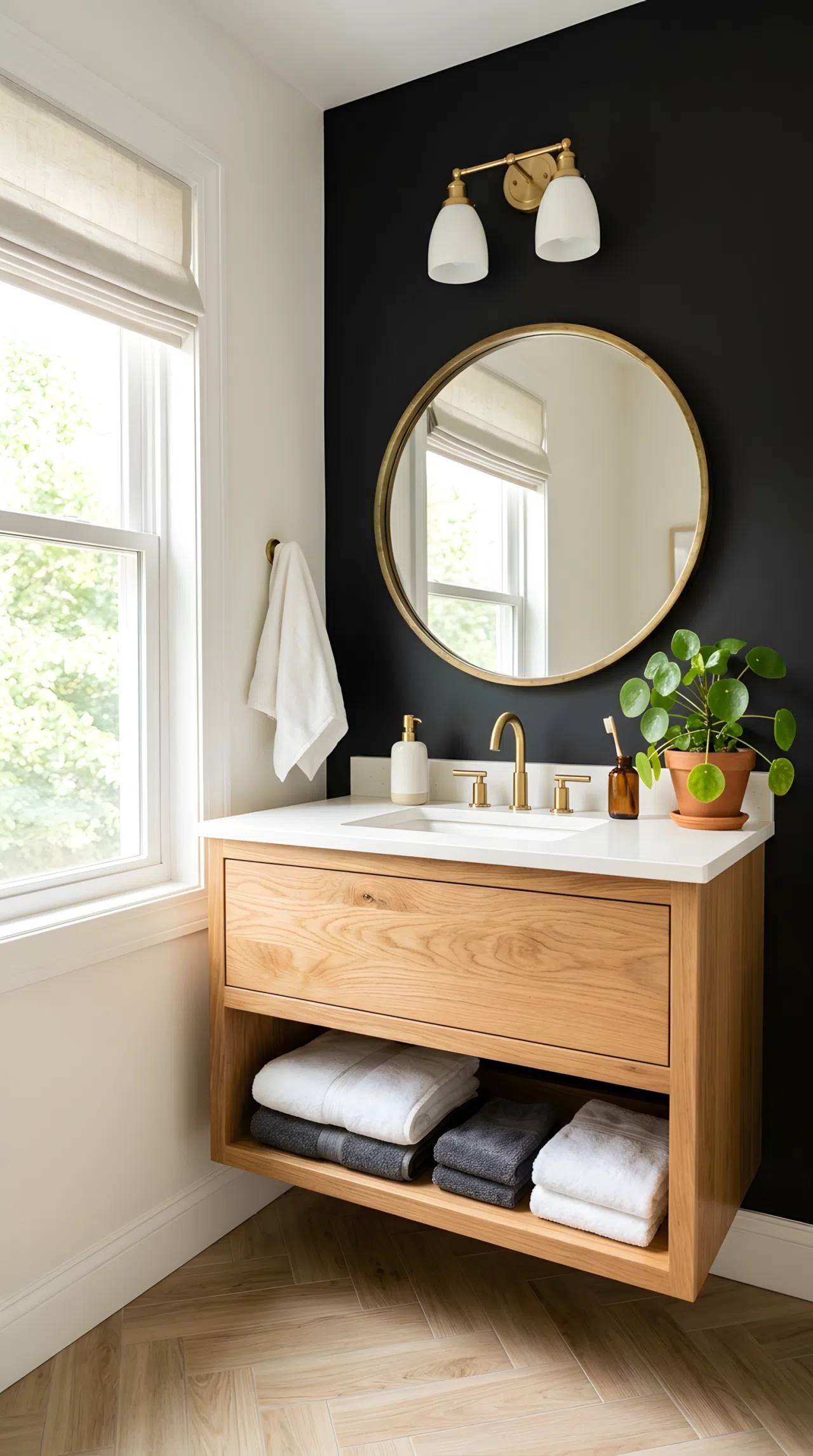 Real-life photograph of a small bathroom with one matte black accent wall (RGB 20,20,20) behind a wood vanity, brass round mirror, neatly made towels, organized counter, clean lines, bright natural light streaming from a side window, vibrant green plant accent, Pinterest-ready styling, photographic stock photo style, no illustration.